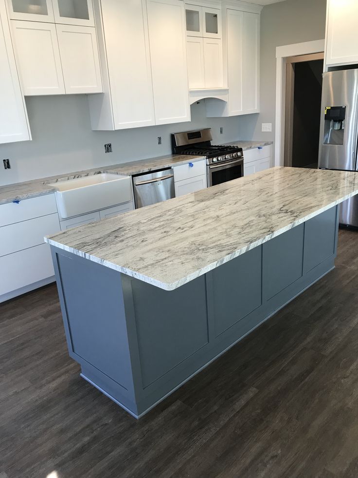 a large kitchen with white cabinets and marble counter tops on the island in front of stainless steel appliances