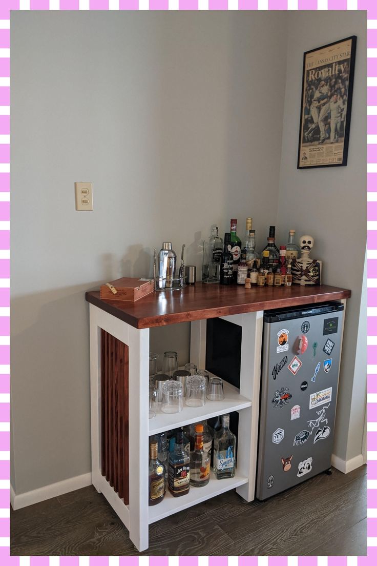 a small bar with liquor bottles and glasses on the top, next to a mini fridge