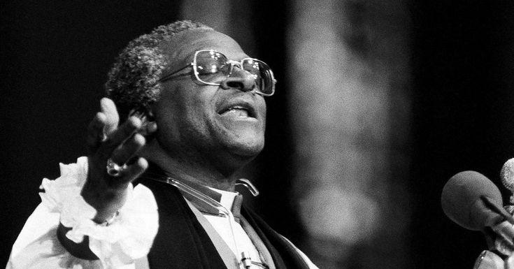 a black and white photo of a man singing into a microphone with his hands in the air