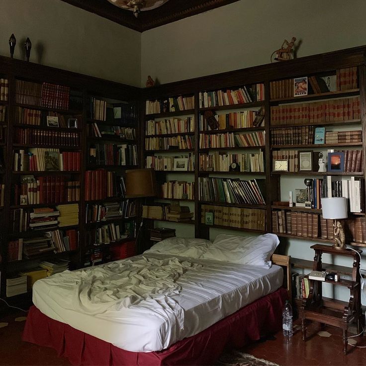 a bed sitting in front of a book shelf filled with books on top of it