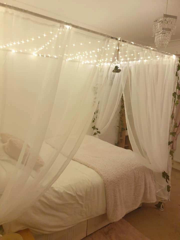 a bed with white curtains and lights hanging from the ceiling