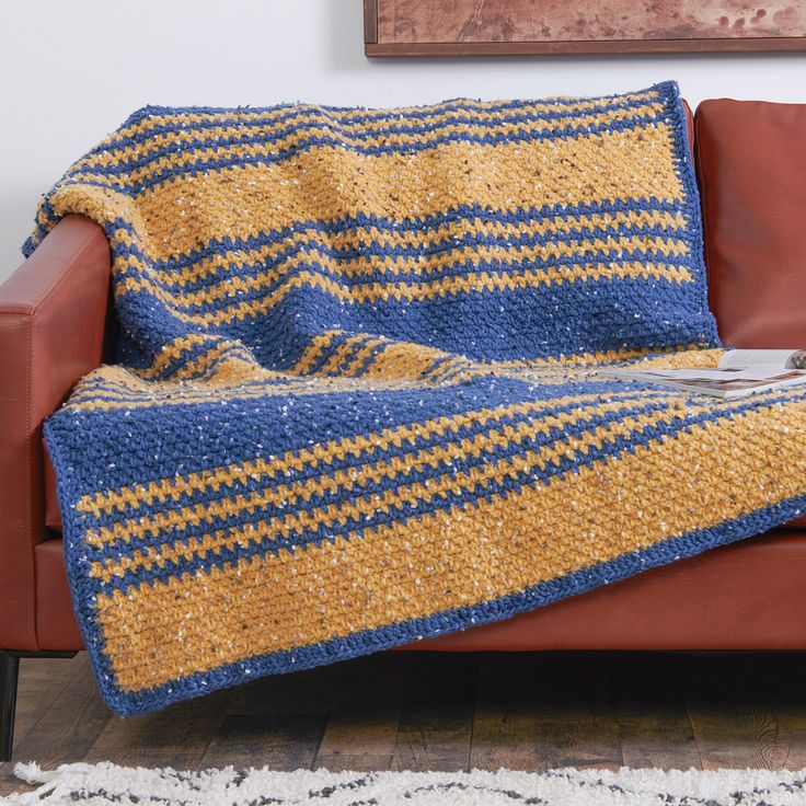 a couch covered in a blue and yellow striped crochet blanket next to a brown leather chair