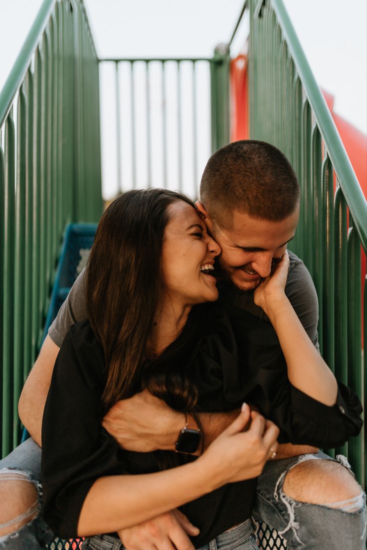 a man and woman cuddling on the steps at an amusement park, one is holding his face to the other's chest