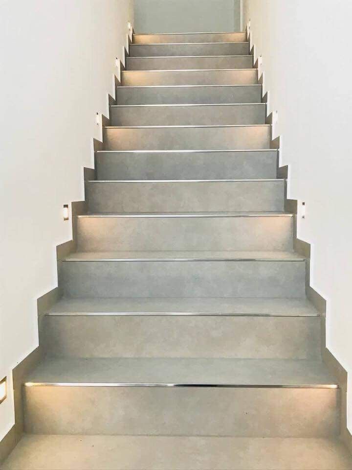 a set of stairs leading up to an open door in a white walled room with light shining on the floor