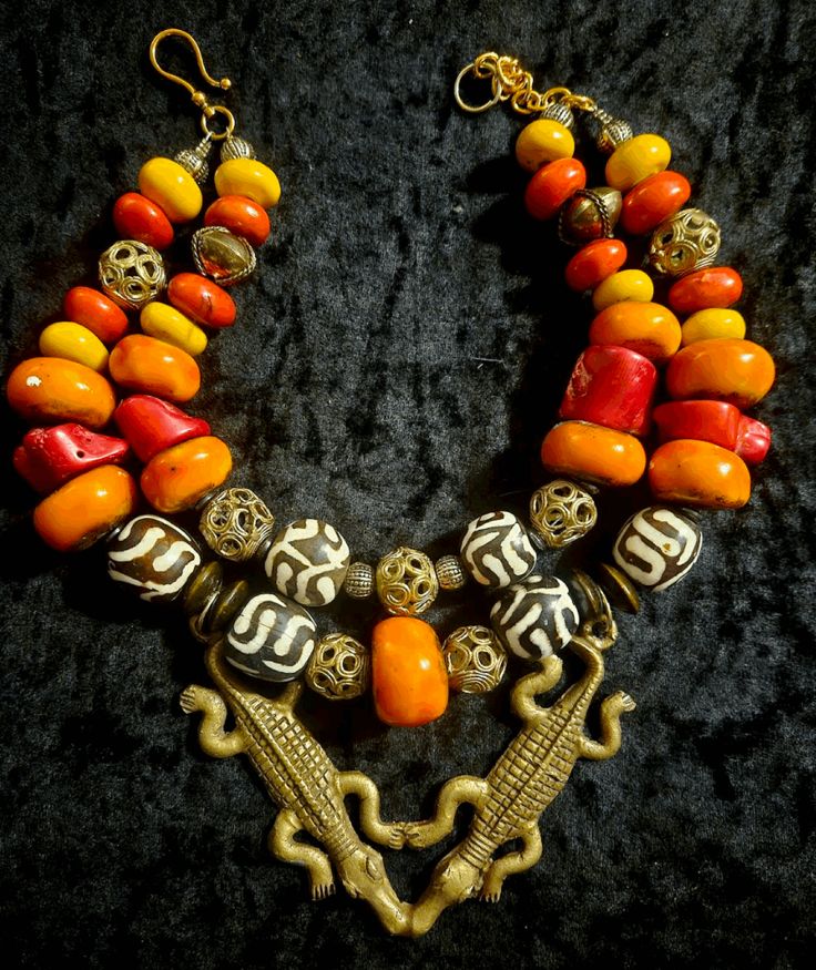 African inspired Tribal jewelry has never looked SO HOT! This double stranded ethnic statement necklace features Moroccan resin, lost wax brass cage work beads, batik zebu bone beads, wood rondelles, vintage brass beads, red branch coral nuggets and other gold tone metals. Adjusting from 17-19", this has a gold tone hook closure and a 2"extender chain which I can lengthen if requested. A very rare double Crocodile or Alligator brass pendant is the focal point and measures 5" x 4.5". A stunning piece worn with a tan or on women of color! From the Atelier of Kat Kouture! Unique Double Strand Beaded Necklaces, Unique Double Strand Beaded Necklace, Traditional Brass Jewelry With Colorful Beads, Traditional Handmade Double Strand Beaded Necklace, Traditional Handmade Double Strand Beaded Necklaces, Traditional Double Strand Beaded Jewelry, Unique Handmade Double Strand Beaded Necklaces, Handmade Unique Double Strand Beaded Necklaces, Unique Ceremonial Jewelry With Large Beads