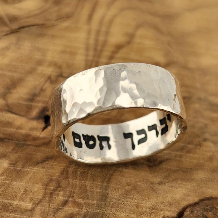 Elevate your style with this Hebrew ring featuring an intricate hammered sterling silver design. Engraved with a secret message from the Bible verse "God bless you and keep you" - "יברכך השם וישמרך" this unique piece exudes elegance and meaning. Perfect for a Jewish wedding band or a meaningful gift. This stunning sterling silver ring is more than just jewelry - it holds the powerful message "This too Shall Pass" from the Song of Solomon. The hammered design adds a touch of uniqueness and charm, making it a meaningful and stylish accessory for any occasion. Embrace tradition with a modern twist with this Hebrew ring crafted from sterling silver. Adorned with a touching Bible verse, "I Am My Beloved," this piece symbolizes love and commitment. Perfect for a Jewish wedding band or as a thoug Hammered Sterling Silver Jewelry For Promise, Adjustable Wide Band Engraved Ring, Promise Sterling Silver Engraved Ring, Promise Sterling Silver Ring With Engraved Text, Sterling Silver Engraved Ring For Anniversary, Anniversary Sterling Silver Engraved Ring With Thick Band, Spiritual Anniversary Engraved Ring, Thick Band Sterling Silver Engraved Ring For Anniversary, Anniversary Engraved Sterling Silver Ring With Thick Band