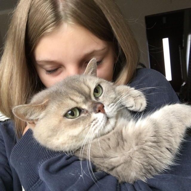 a woman holding a cat in her arms and looking at it's face with eyes wide open