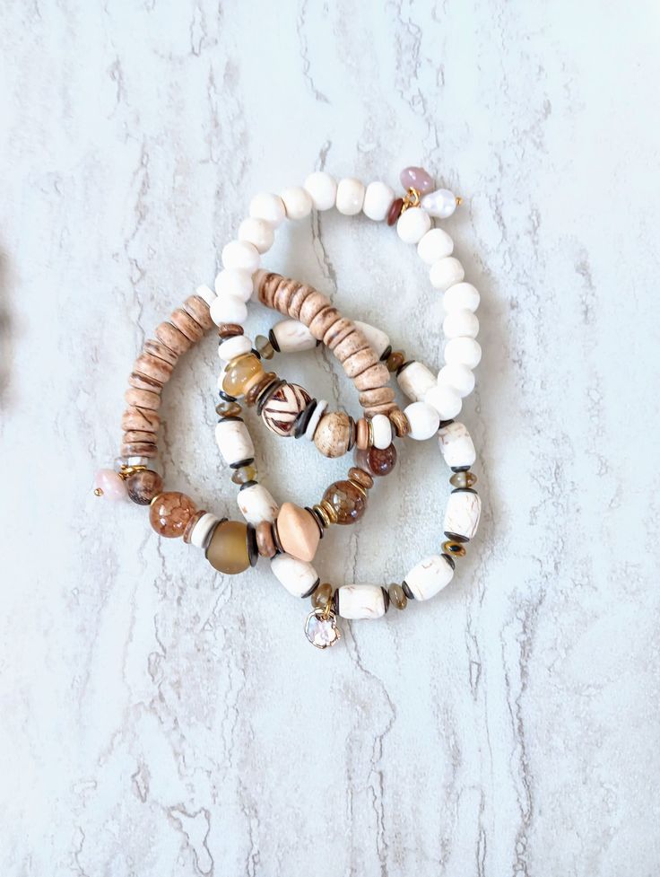 Soft, serene, cozy, and beachy. Beautiful beige, white, caramel, brown, and ecru in these mixed medium stack bracelets. Several white Howlite, White Turquoise, Quartz, and more. Gemstone beads in different sizes and colors. Creamy alabaster ethical bone beads, matte sea shells, white and natural coconut disk beads, rustic antique beads, and African recycled glass. Mix in with an array of mixed metals, and cluster accents of mixed gemstone beads including pearls. Unique and stunning. The item/s p Brown Beaded Bracelets With Natural Stones For Beach, Brown Natural Stones Beaded Bracelets For Beach, Brown Natural Stone Beaded Bracelets For Beach, White Bohemian Jewelry With Wooden Beads, Bohemian White Jewelry With Wooden Beads, Bohemian Beige Bracelet For Festivals, Earthy Beaded Bracelets For Beach, Earthy Natural Stone Beaded Bracelets For Beach, Earthy Hand Wrapped Bracelets For Beach