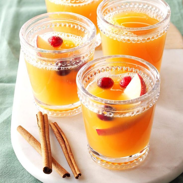 four glasses filled with orange juice and topped with cinnamon sticks on a white platter