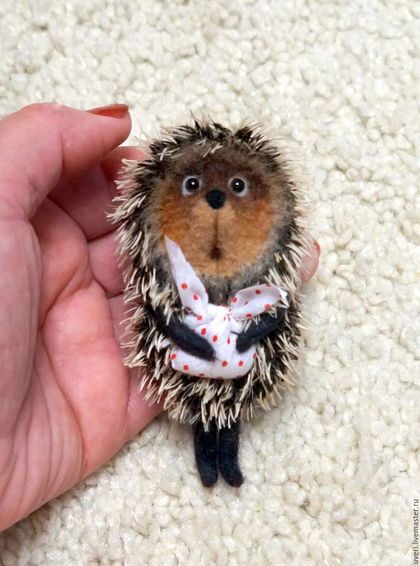 a hand holding a tiny toy hedgehog wearing a white shirt and red polka dot tie