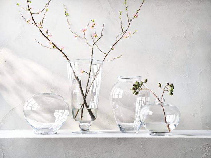 three clear vases with flowers in them on a shelf next to a white wall