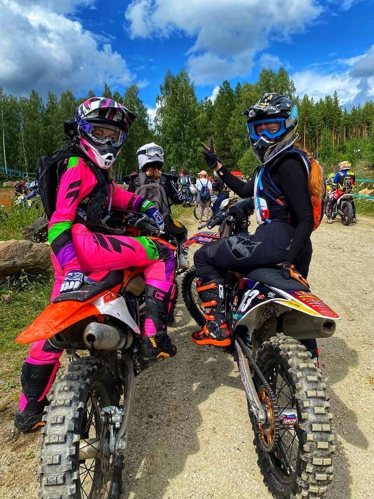 two people sitting on dirt bikes with helmets on and one person standing next to them