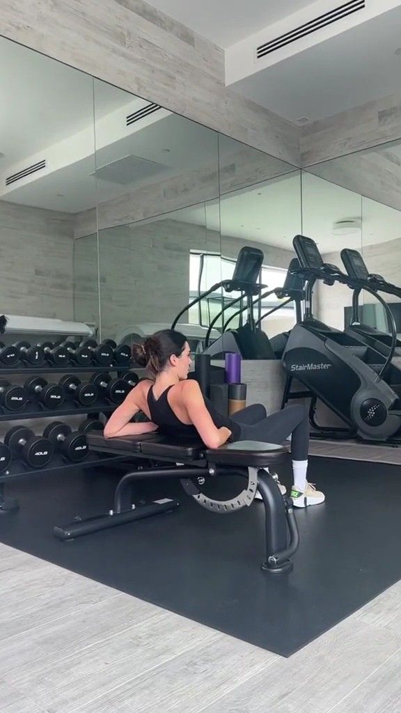 a woman sitting on a bench in front of a gym with exercise equipment and mirrors