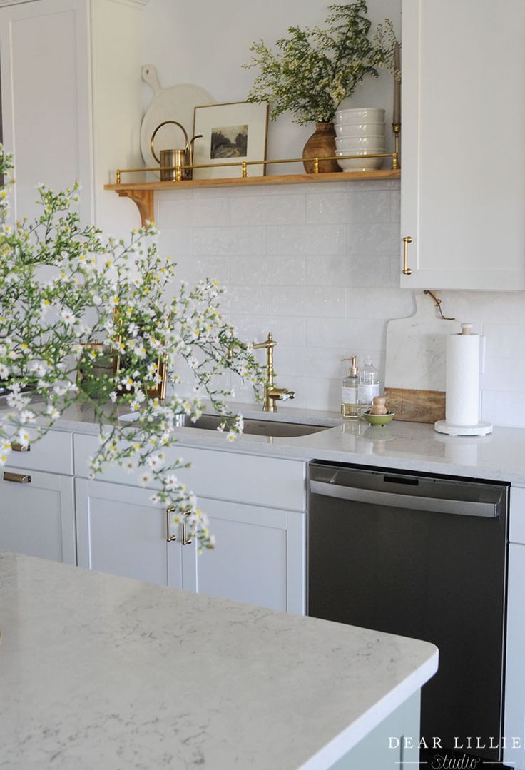 a white kitchen with marble counter tops and gold trimmings on the shelves above the sink