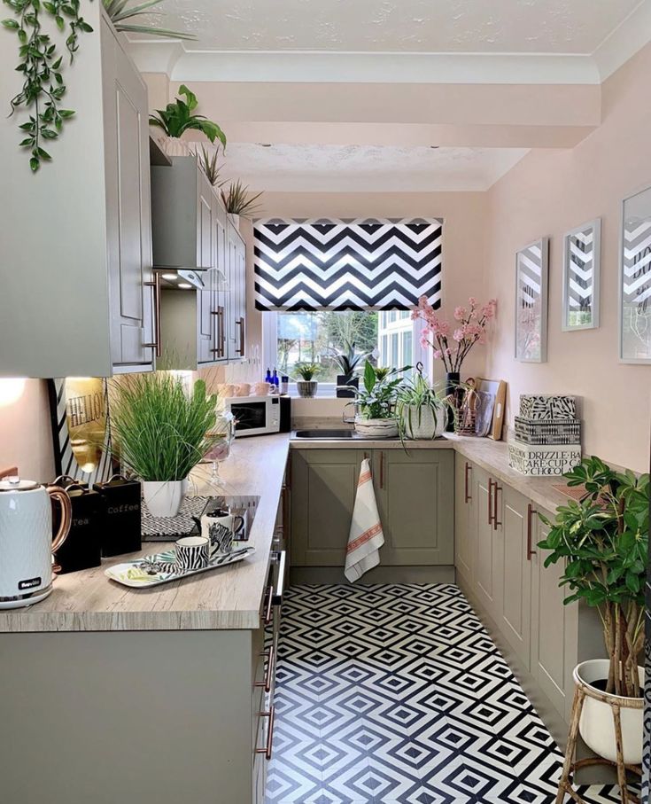 a kitchen with black and white tile flooring, potted plants and pictures on the wall