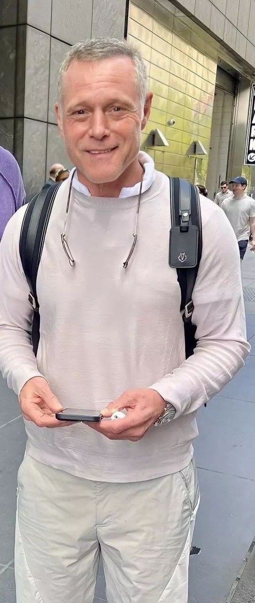 a man in white is holding his cell phone and smiling at the camera while standing outside