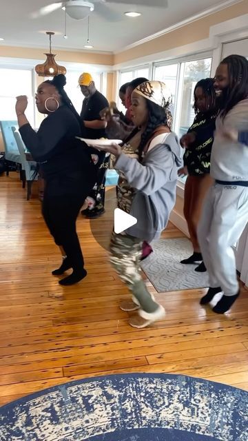 group of people dancing in a living room with wooden floors and large windows on the wall