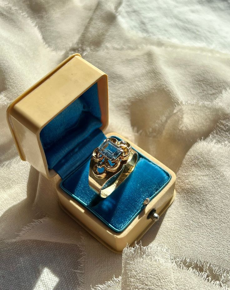 ◆Materials: Blue Topaz, 18k Yellow Gold  ◆Gems: Blue Topaz ◆Size: US 10 (easily sizable by your jeweler) ◆Measurements: All approximate - blue topaz 5.9mm x 7.9mm; center band width 12.4mm; back of the band 4.2mm; rise above finger 4.7mm  ◆Weight: 5.5g ◆Hallmarks: '750' (for 18k); possibly maker's mark 'NW' A gorgeous vintage ring featuring a pale blue rectangular step-cut blue topaz. It's set on an open and raised quatrefoil design with two small beads decorating the east and west sides of the Gold Jewelry With Rose Cut Diamonds And Blue Topaz, Rectangular Topaz Ring Fine Jewelry Gift, Fine Jewelry Topaz Ring With Rectangular Stone For Gift, Rectangular Topaz Ring As Gift, Fine Jewelry Style, Fine Jewelry Rose Cut Diamond Rectangular Rings, Rectangular Topaz Ring In Yellow Gold, Blue Topaz Baguette Cut Jewelry For Wedding, Yellow Gold Blue Topaz Rings With Emerald Cut, Wedding Jewelry With Baguette Cut Blue Topaz