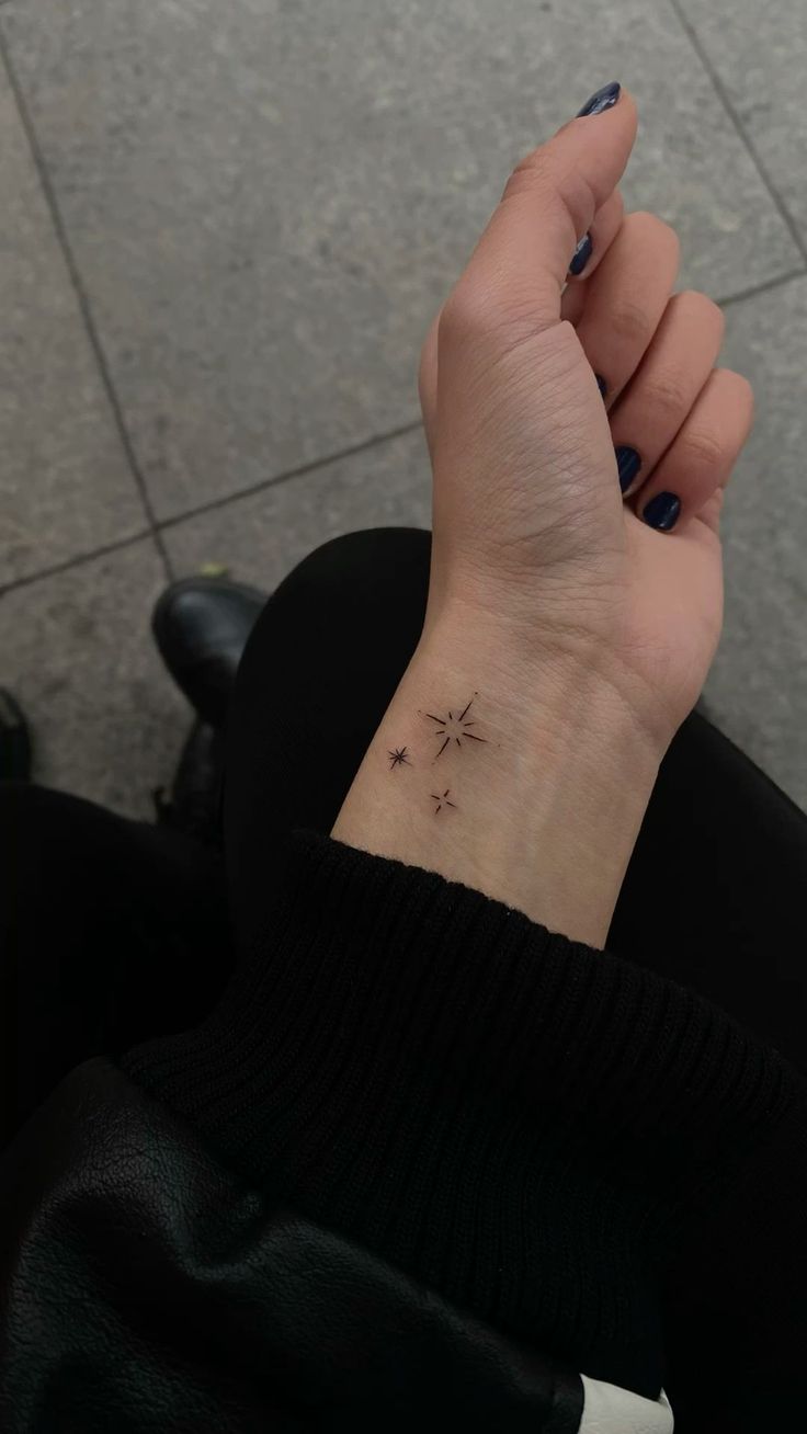 a woman's hand with a small star tattoo on it, sitting in front of a tile floor