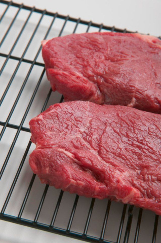 two pieces of raw meat sitting on top of a metal grill grate next to each other