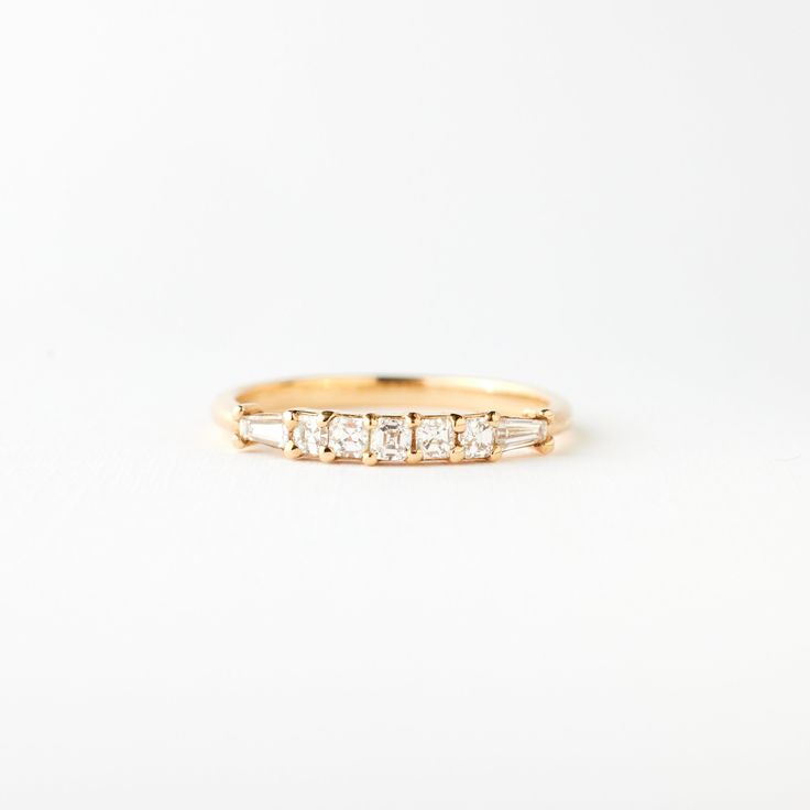 a yellow gold ring with five baguettes of diamonds on the side, set against a plain white background