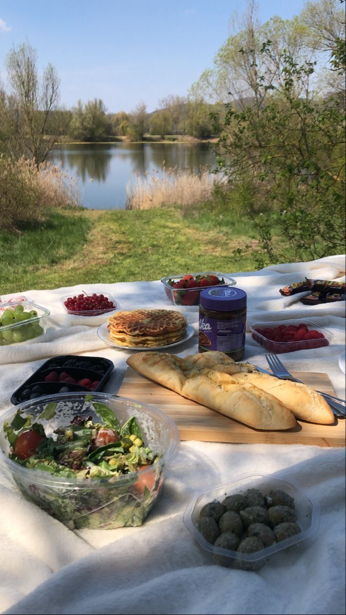 a picnic table with bread, salad and fruit on it near the water's edge