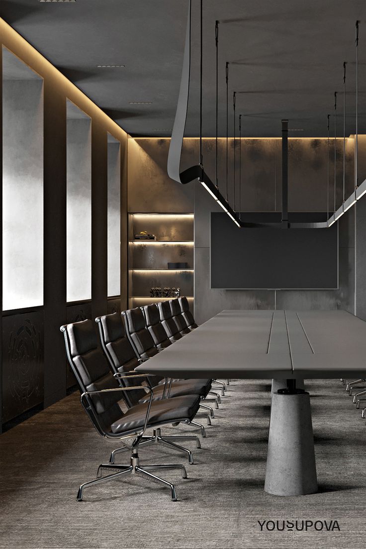 an empty conference room with long tables and chairs in the foreground is lit by recessed lighting