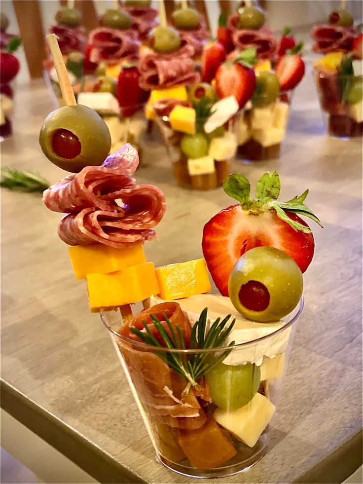 an assortment of appetizers are arranged in cups on a table with olives, strawberries and cheese