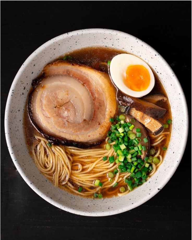 a white bowl filled with noodles, meat and an boiled egg on top of it