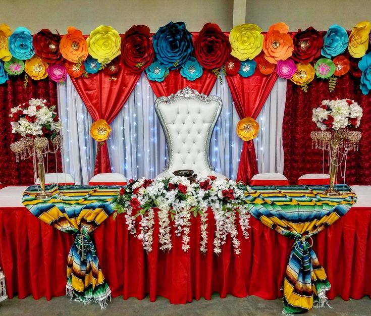 a decorated banquet table with red, yellow and blue flowers on the headpieces