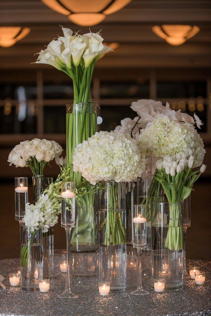 there are many vases with flowers and candles in them on the table next to each other