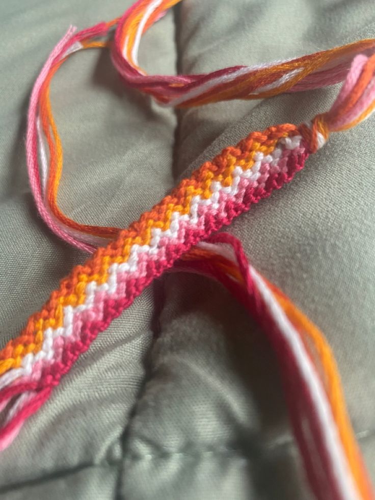 an orange and pink crocheted object laying on top of a gray bed sheet