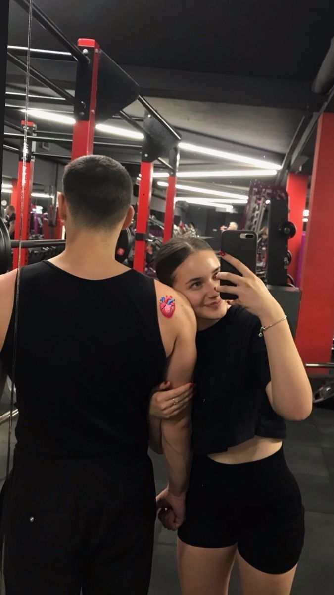 a man and woman standing next to each other in a gym together, taking pictures with their cell phones