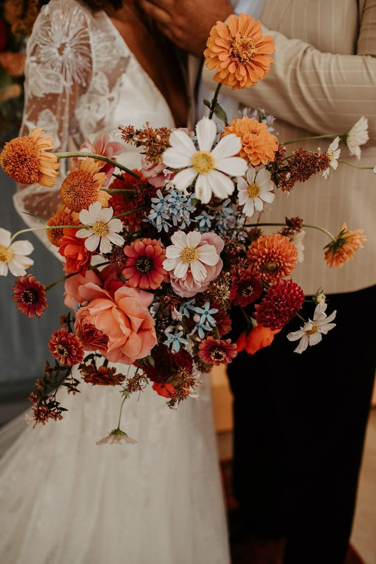 the bride and groom are kissing in front of an orange flower bouquet on their wedding day