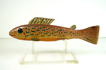 a wooden fish on a clear stand with white wall in the backgroung