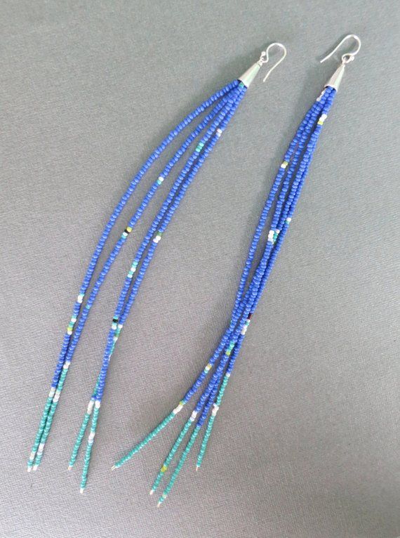 two pairs of blue beaded earrings on a gray surface with beads hanging from them