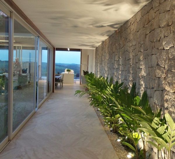 a long hallway with plants on both sides and glass doors leading to the outside area