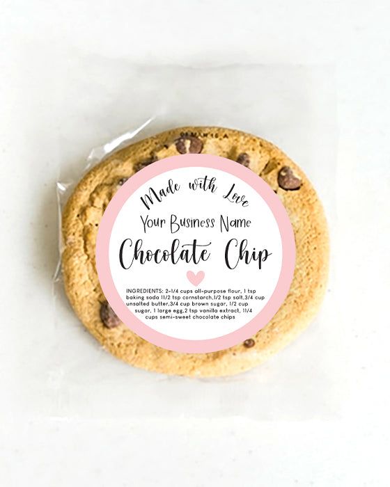 a chocolate chip cookie with pink and white labels on the top, sitting on a piece of parchment paper