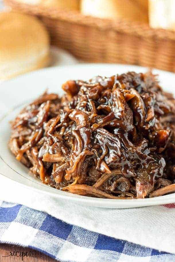 a white plate topped with shredded beef on top of a blue and white checkered table cloth