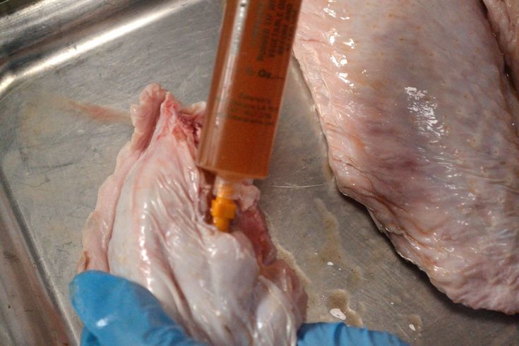 a person in blue gloves is holding a bottle with liquid on it next to meat