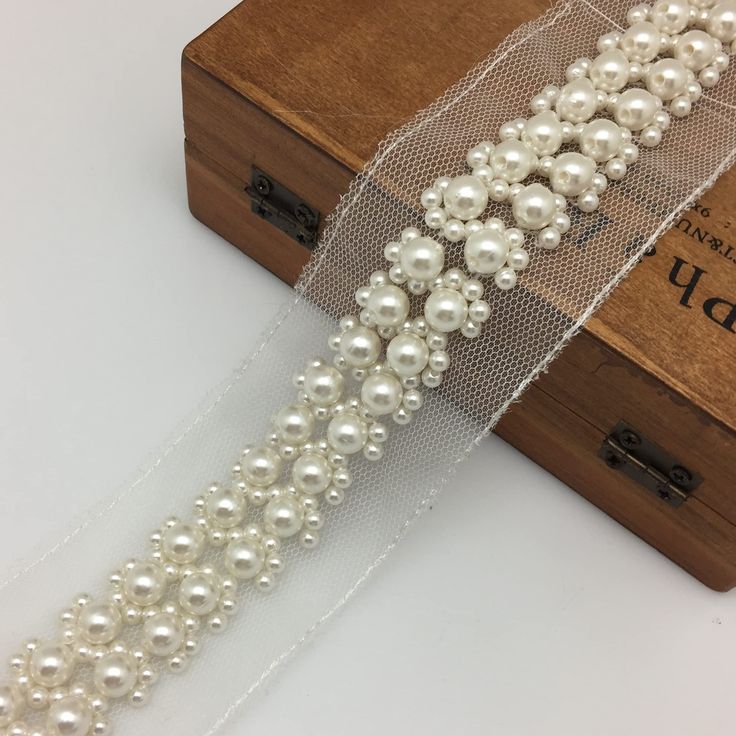 a white ribbon with pearls on it next to a wooden box and some other items