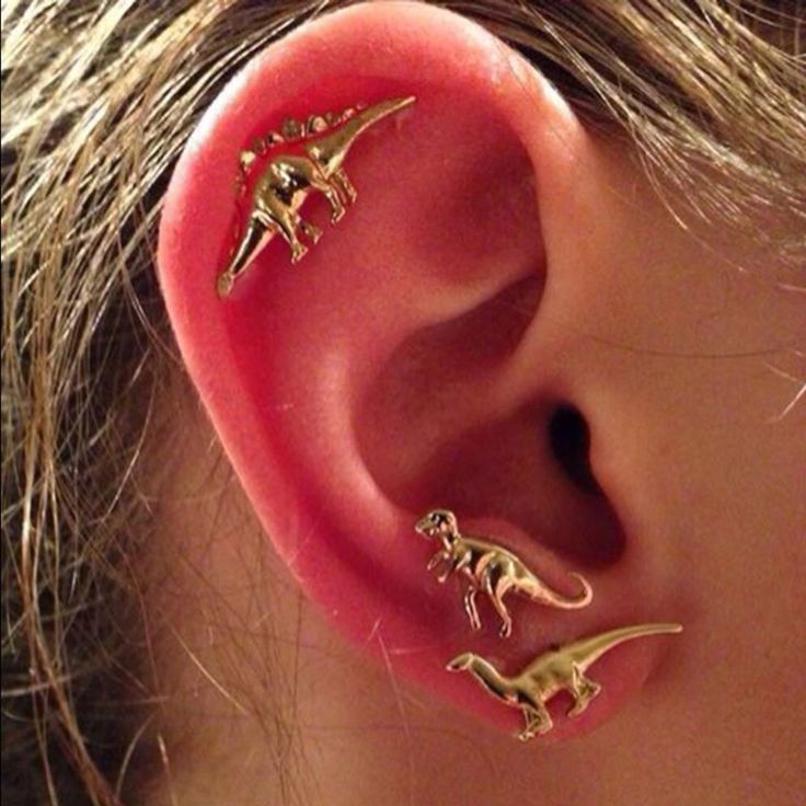 three small dinosaurs are attached to the side of a woman's ear with gold colored posts