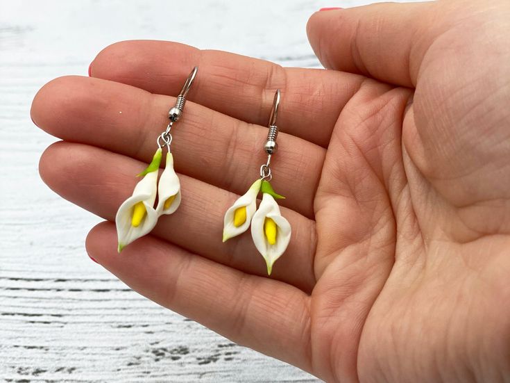 a hand holding two white and yellow flowers in it's left earrings