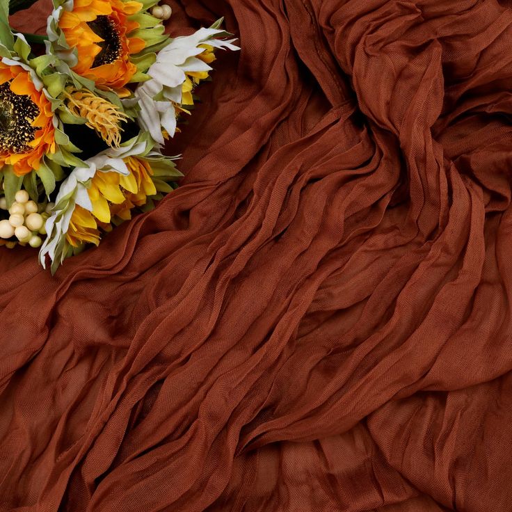 sunflowers and other flowers are laying on a brown sheet that is draped over