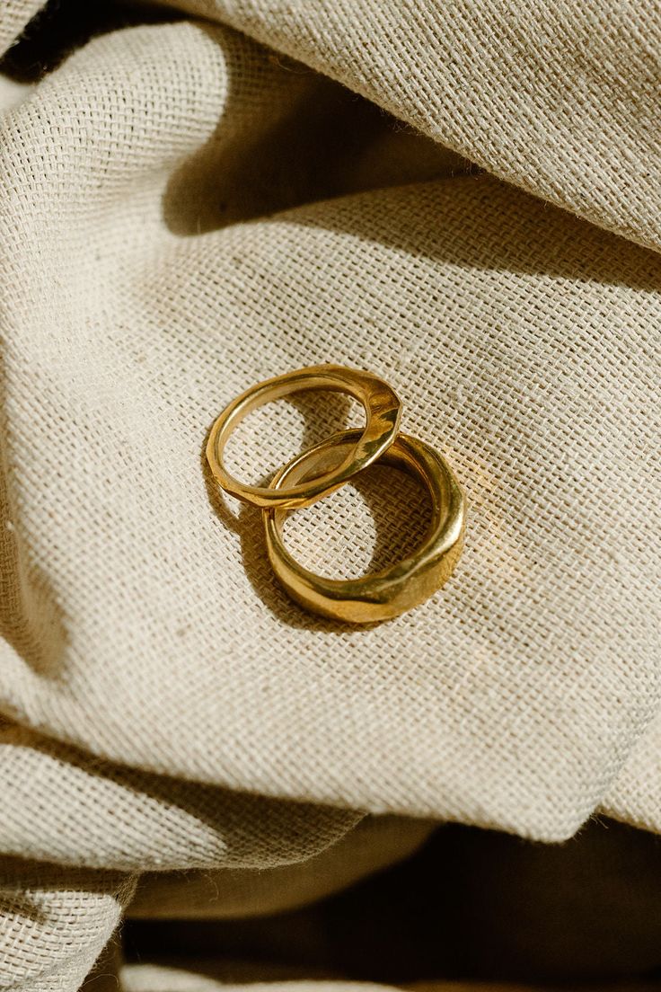 two gold rings sitting on top of a white cloth covered in burlocked material