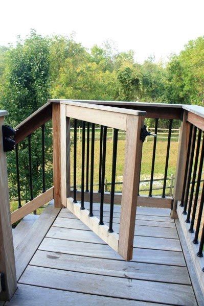 a wooden deck with railings leading to a grassy area and trees in the background