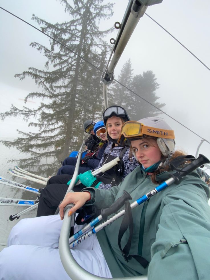 two women riding on a ski lift in the snow with their skis and poles