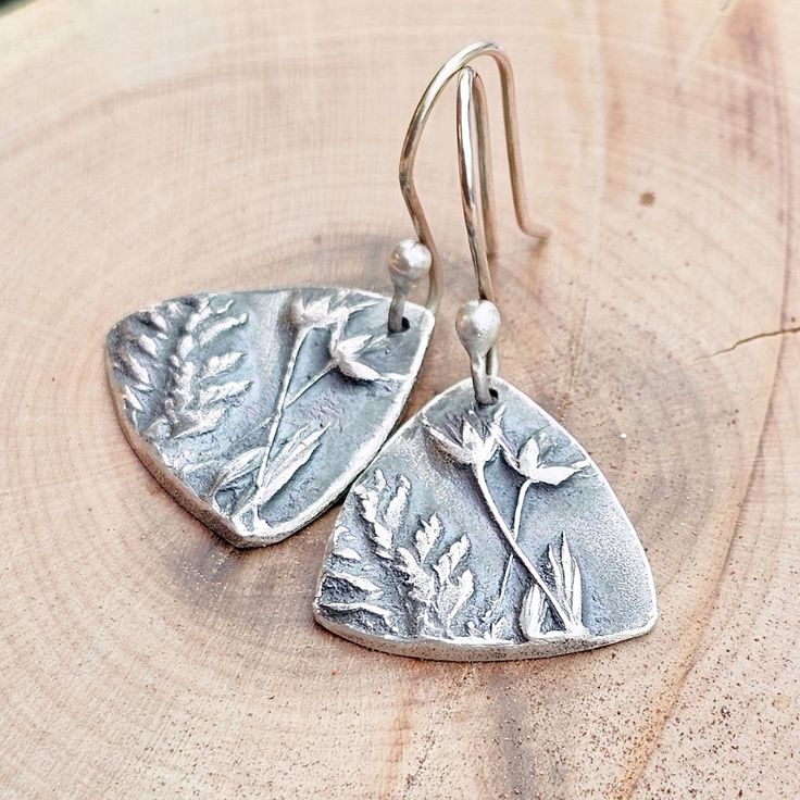 These sterling silver wildflower earrings are made from a one-of-a-kind mold. The mold was created using wildflowers on the edge of the forest in N MN. Precious metal clay is rolled and pressed into the mold, sanded, and then fired in a high-temp kiln. All of the organic binders burn off and the remaining piece is 92.5 sterling silver.  The edges of the earrings have been lightly pounded with a hammer. The piece has been oxidized and then brushed and burnished to bring out the details of the flowers. They hang 1 5/8 inches from the top of the ear wire to the bottom of the triangle. The ear wires are hand-made from torch-balled sterling silver. All materials used come from a recycled silver source.  All pieces come in an eco-friendly Kraft box. Gift wrap options are available. Thank you for Silver Sterling Silver Earrings With Pressed Flowers, Handmade Nature-inspired Flower Earrings, Nature-inspired Flower Earrings, Nature-inspired Birth Flower Earrings, Nature-inspired Dangle Flower Earrings, Nature-inspired Sterling Silver Earrings, Handmade Silver Botanical Earrings, Nature-inspired Sterling Silver Flower Earrings Nickel Free, Nature-inspired Silver Flower Drop Earrings