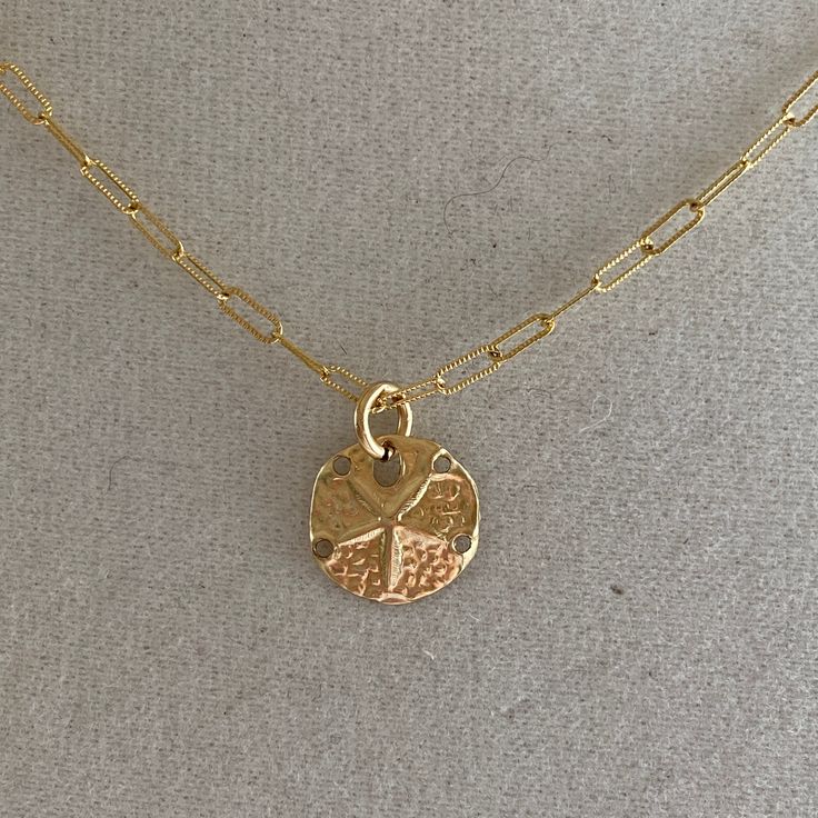 A sand dollar coin dangles from a delicate gold chain. The chain measures approximately 17 inches long is adjustable up to an inch shorter. Adjustable Gold Medallion Charm Necklaces, Gold Adjustable Round Disc Charm Necklaces, Gold Medallion Charm Necklace, Gold Coin Necklace With Adjustable Chain For Everyday, Adjustable Gold Medallion Necklace With Round Pendant, Adjustable Gold Medallion Necklace, Adjustable Gold Coin Necklace, Gold Adjustable Medallion Necklace With Round Pendant, Nickel-free Yellow Gold Medallion Coin Necklace