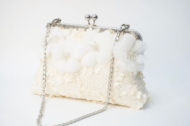 a white purse with flowers on the front and chain at the bottom, sitting on a white surface